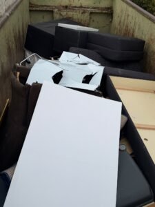 Entsorgung von Sperrmüll nach einer Entrümpelung in Frankfurt: Container mit dunklen Polstermöbeln und weißen Möbelplatten