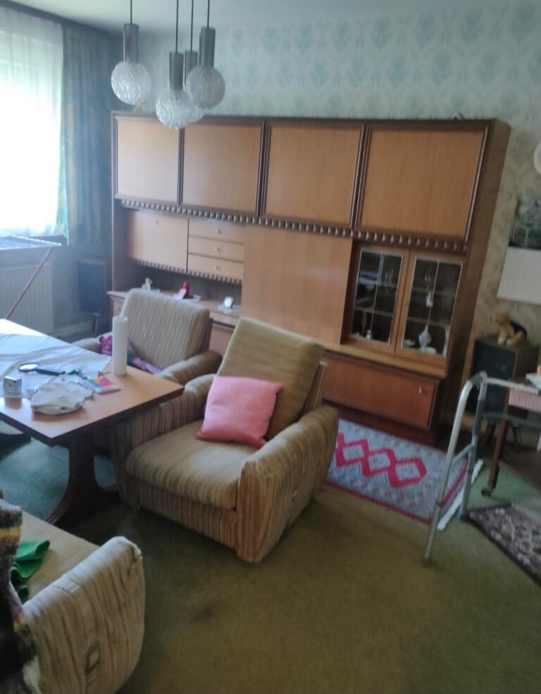 Haushaltsauflösung vorher: Wohnzimmer mit Schrankwand, Sesseln, Teppichboden und Vorhängen